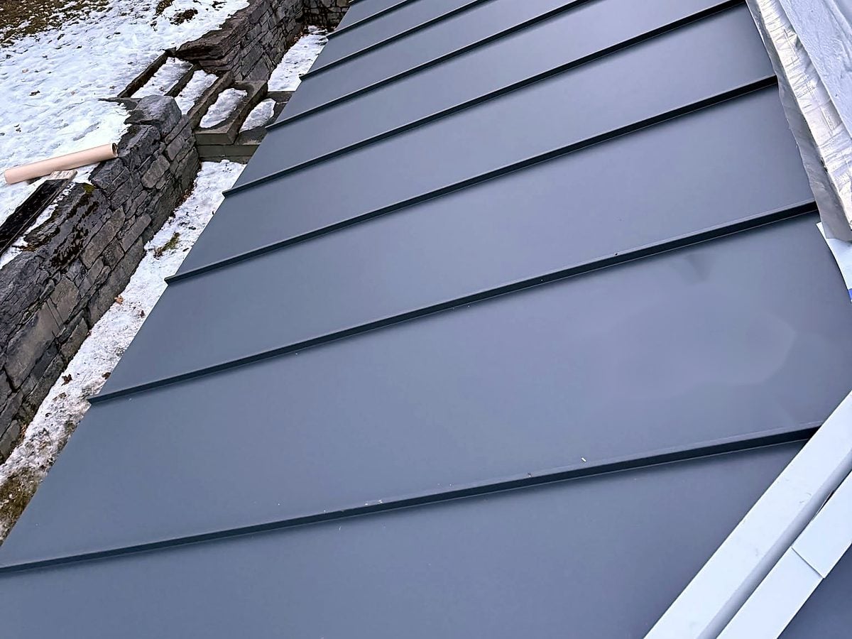 Standing seam metal roof beside a snow-covered yard